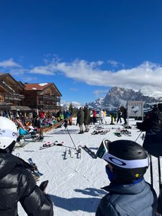 skiers and snowboarders at the bottom of a ski slope with mountains in the background