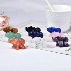 small glass elephants sitting on top of a table next to a white cup and spoon