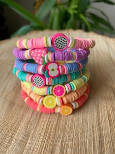 a stack of colorful bracelets sitting on top of a wooden table next to a potted plant