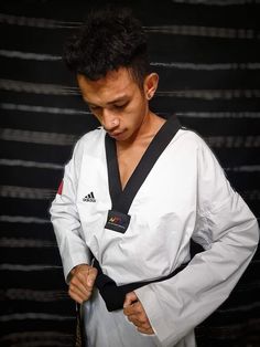 a man standing in front of a black wall with his hands on his hips wearing a white karate suit