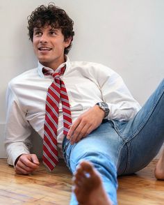 a man wearing a red and white striped tie sitting on the floor with his feet up