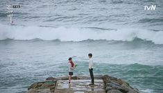 two people standing on rocks near the ocean