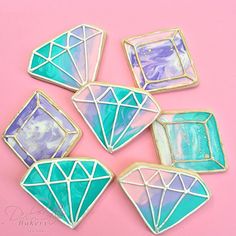 four decorated sugar cookies with blue and green icing on pink background, one is cut in half to look like diamonds