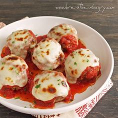 a white bowl filled with meatballs covered in sauce on top of a wooden table