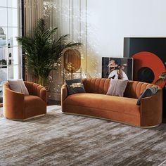 a living room with two orange couches in front of a large painting on the wall