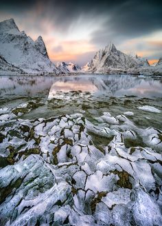 the mountains are covered in snow and ice as the sun is setting over a lake