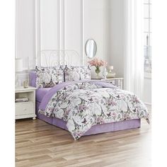 a bed with purple and white comforters in a room next to a mirror on the wall