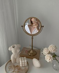 a mirror sitting on top of a white table next to flowers and rings in front of it