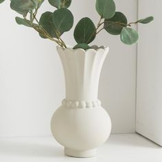 a white vase with some green leaves in it