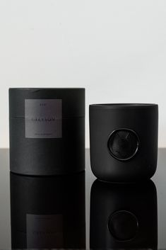 two black containers sitting next to each other on top of a glass table with a white wall in the background