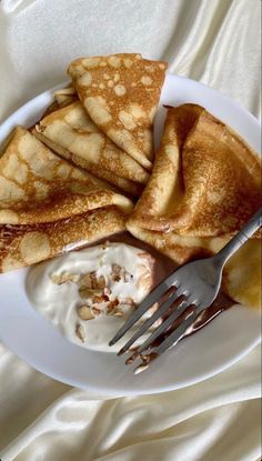 pancakes and whipped cream on a white plate with a fork in the middle, sitting on a bed