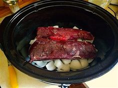 two pieces of meat in a slow cooker with onions and potatoes on the side