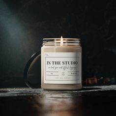 a candle sitting on top of a wooden table next to a black mug with the words in the studio printed on it