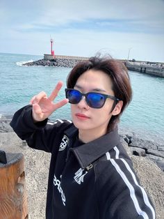 a woman wearing sunglasses making the peace sign with her hand while standing next to the ocean