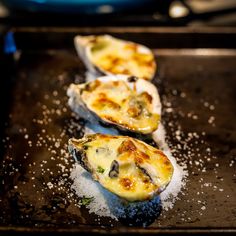 three cooked oysters sitting on top of a baking sheet covered in salt and pepper