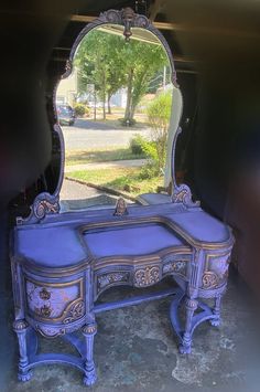 a blue vanity with a mirror on it in front of a driveway and trees behind it