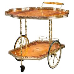 an ornately designed serving cart with wheels and wooden handles, painted in gold leaf