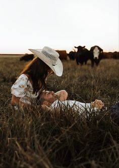 a woman sitting in the grass with cows behind her