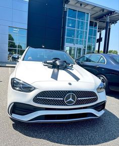 a white car with a black bow on it's hood parked in front of a building