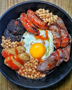 a black bowl filled with sausages, beans and an egg