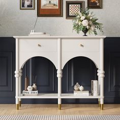 a white console table with gold legs in front of a blue wall and pictures on the wall