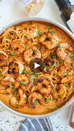 a pan filled with shrimp and pasta next to bottles of wine