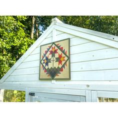 an old quilt hanging on the side of a white building with trees in the background