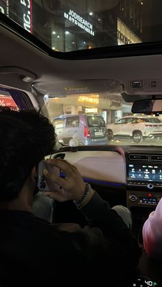 two people sitting in the driver's seat of a car, looking at their cell phones