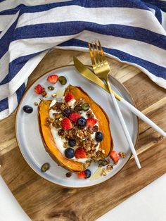 a white plate topped with fruit and granola on top of a wooden cutting board