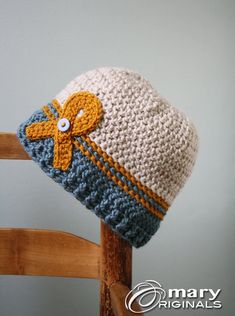 a crocheted hat with an orange and blue bow on it sitting on top of a wooden chair