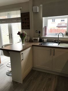 a kitchen with wooden floors and white cabinets, an island countertop and sink in front of a window