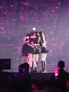 three girls hugging each other on stage with confetti in the air behind them