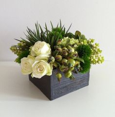 an arrangement of white flowers and succulents in a wooden box on a table