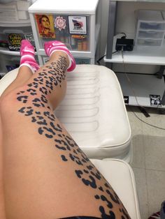 a woman's legs with black and white tattoos on them, sitting in front of a freezer