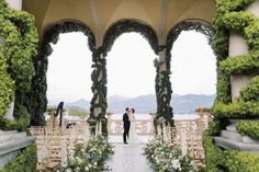 a bride and groom standing in front of an archway with greenery on either side