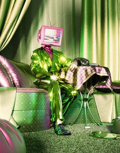 a man sitting on top of a green couch in front of a tv monitor and chair