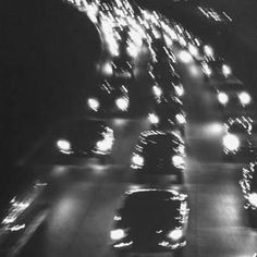 black and white photograph of cars driving down a highway at night with lots of lights