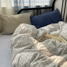 an unmade bed with two pillows and a book on the pillowcase next to it