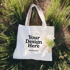 a white tote bag laying in the grass with your design here printed on it