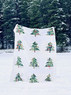 a white blanket with trees on it sitting in the snow next to some pine trees