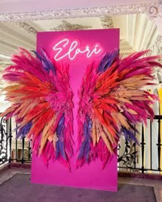 a pink sign with purple and red feathers hanging from it's side in front of a balcony