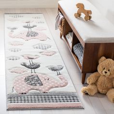 a teddy bear sitting on the floor next to a rug with an elephant and bird design