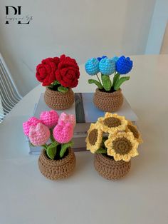 four crocheted flowers in small pots on a table