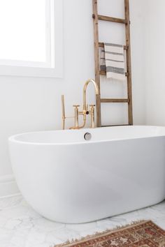 a white bath tub sitting in a bathroom next to a rug on the floor and a window