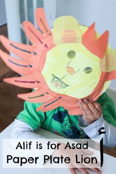 a child's hand holding up a paper plate lion mask with the words, alif is for asad paper plate lion