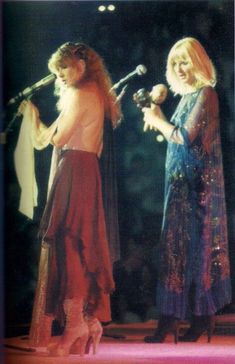 two women are standing on stage with microphones in their hands and one is wearing a long dress