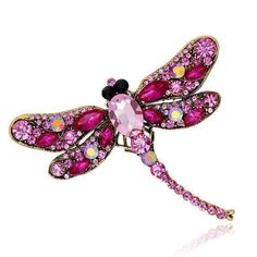 a pink dragonfly brooch sitting on top of a white table next to a mirror