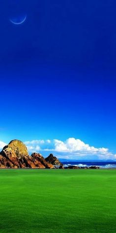 a green field with mountains in the background and a blue sky above it that has a half moon