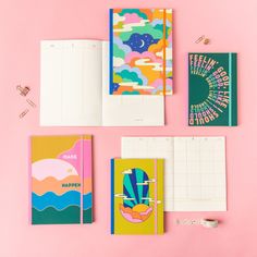 three notebooks with colorful covers on a pink surface next to an open planner book