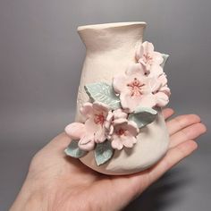 a hand holding a ceramic vase with flowers on it